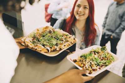 Female assistant giving food plate to smiling female customer in city