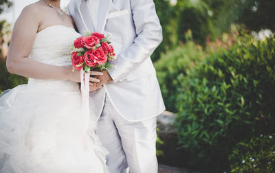 Midsection of bride and bridegroom holding bouquet on field