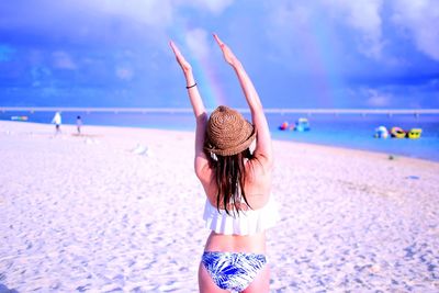 Rear view of woman gesturing while standing at beach against sky
