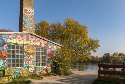 Graffiti on building by river against clear sky