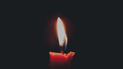 Close-up of burning candle against black background