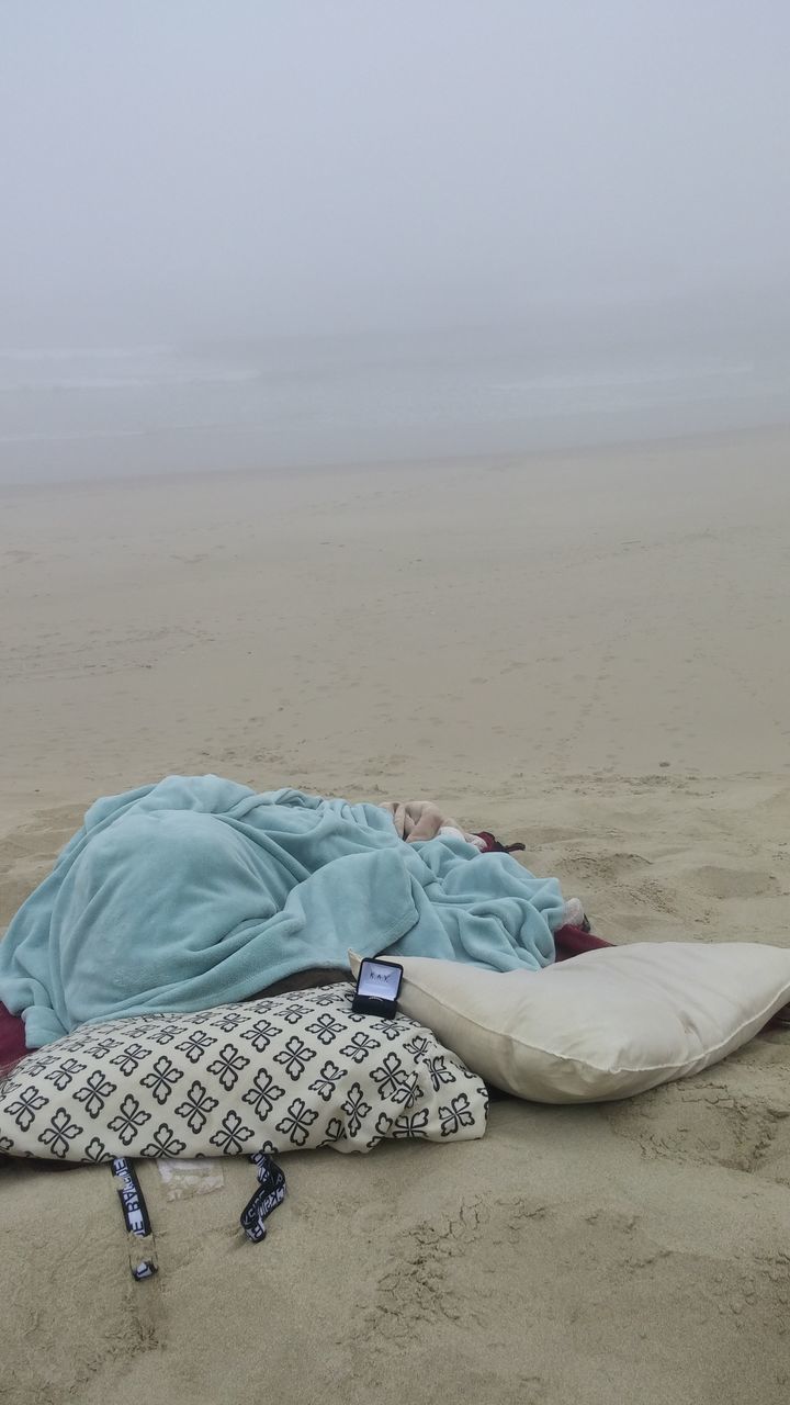 MAN LYING DOWN ON BEACH AGAINST SKY