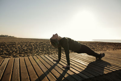 Woman doing yoga at beach against clear sky