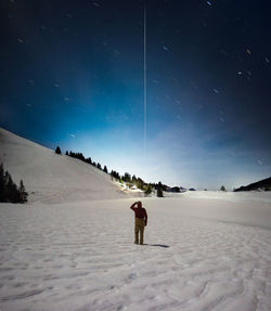 Full length of person standing on snow covered land against star trails at night