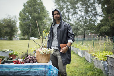 Portrait of mid adult man standing by freshly harvested vegetables on table at urban garden