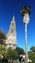 Low angle view of historic church and palm tree against clear blue sky