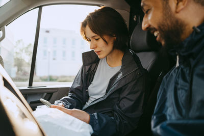 Female delivery person using smart phone while sitting with male coworker in van