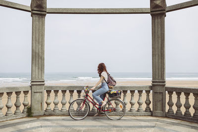 Woman looking at sea while sitting on bicycle near retaining wall