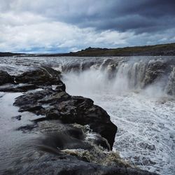 Scenic view of waterfall against cloudy sky