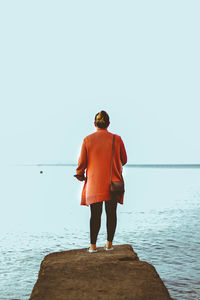 Rear view of man standing on sea against clear sky