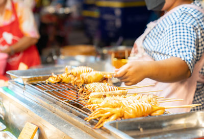 Woman grilled squid in a stick at the street food market.