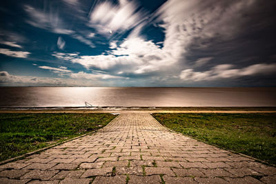 Footpath leading towards sea against sky