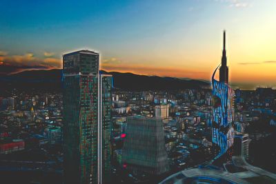 Illuminated buildings in city against sky during sunset