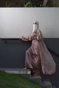 Full length view of veiled woman with white niqab and pink silky dress walking up the stairs