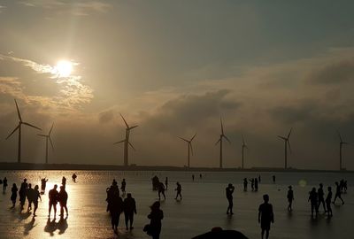 Group of silhouette people on beach against sky during sunset