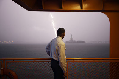 Businessman looking at statue of liberty while standing by railing on ferry during stormy weather