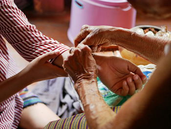 Midsection of senior woman tying string on granddaughter hand