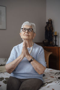 Senior woman with hands clasped sitting on bed at home