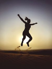 Silhouette woman jumping against sky during sunset