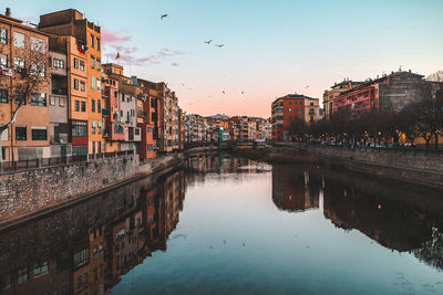 Reflection of buildings in town against sky at sunset
