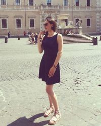 Full length portrait of young woman standing on street in city