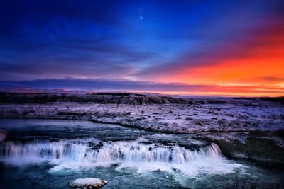 Scenic view of waterfall against sky during sunset