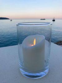 Close-up of tea light candle on table against sea