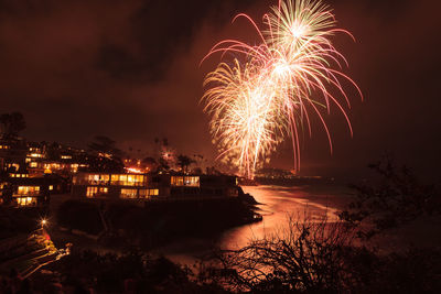 Illuminated fireworks over beach against sky in city at night