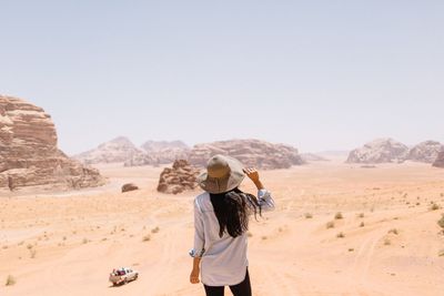 Rear view of woman standing at desert against clear sky