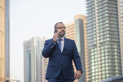 Businessman using mobile phone while standing against buildings in city