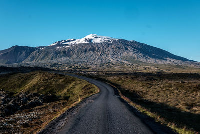 Road amidst snowcapped mountains against clear blue sky