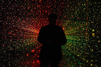 Rear view of silhouette man standing against illuminated tree at night