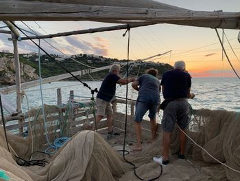 Rear view of people standing on sea shore against sky during sunset