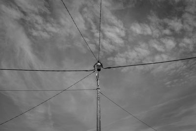 Low angle view of street light attached to power lines against cloudy sky