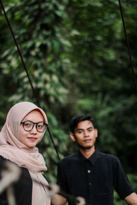 Portrait of young man with girlfriend standing on footbridge in forest