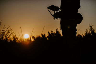 Silhouette man photographing on field against sky during sunset