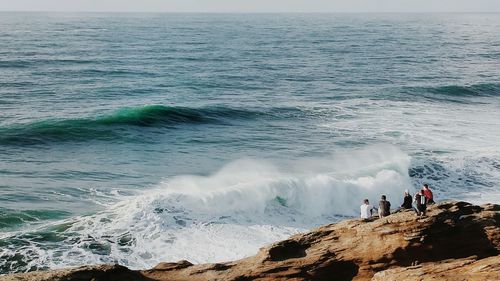 Rear view of friend relaxing on rock formation against sea