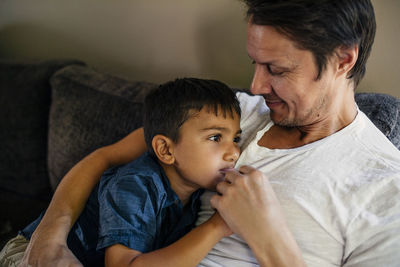 Smiling father with son sitting on sofa at home