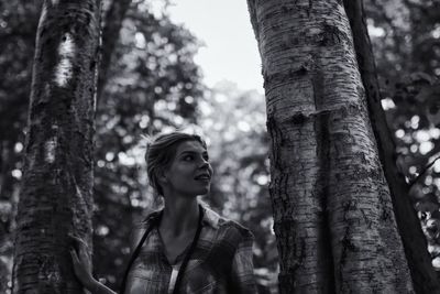 Thoughtful young woman standing amidst tree trunks