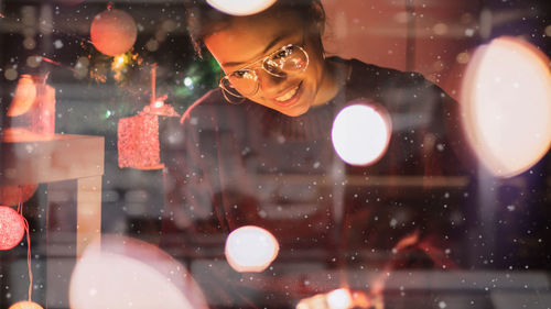 Smiling mid adult woman seen through glass window in illuminated house during christmas night