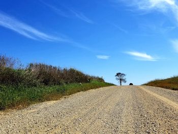 Dirt road amidst field against sky