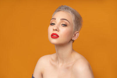 Close-up portrait of young woman against orange background