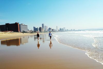 People walking at beach against clear sky