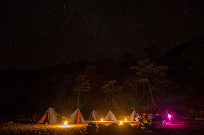 Illuminated lighting equipment by tents against sky at night