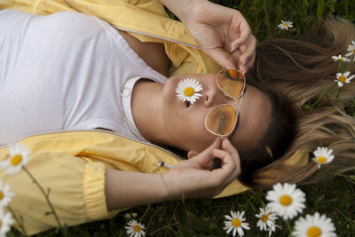 High angle view of woman lying amidst daisies on field