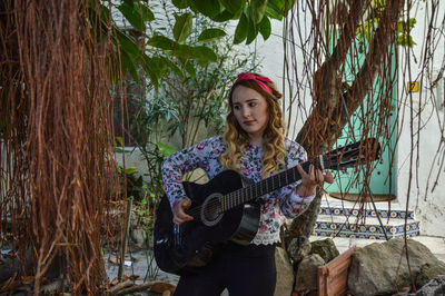 Young woman playing guitar outside house