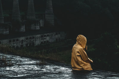 Rear view of person in raincoat sitting on rooftop