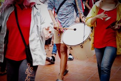 Midsection of man playing drum amidst crowd on footpath during festival