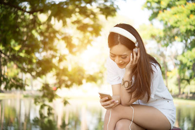 Young woman using mobile phone while sitting against lake