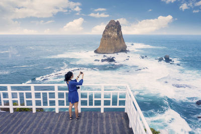 Young woman photographing sea against sky